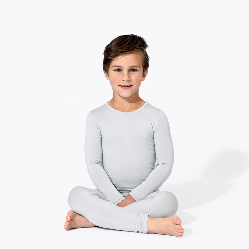 Child sitting cross-legged in a light grey long-sleeve pajama top and matching pants.