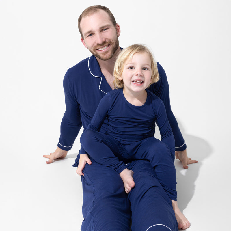 An adult and child sitting together in solid blue pajamas, with a button-front adult top and a pullover child’s top.