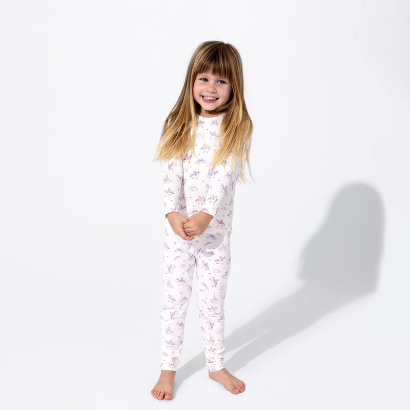 Child standing barefoot in white Unicorn-print long-sleeve pajamas against a white background.