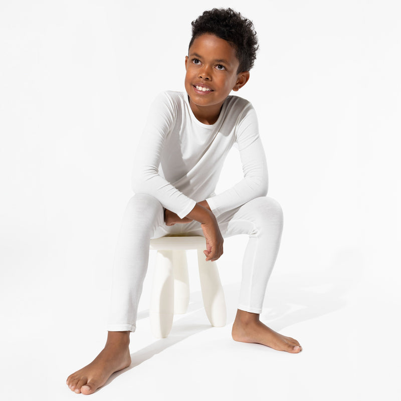 Child wearing Milk White long-sleeve pajamas while sitting on a white stool.