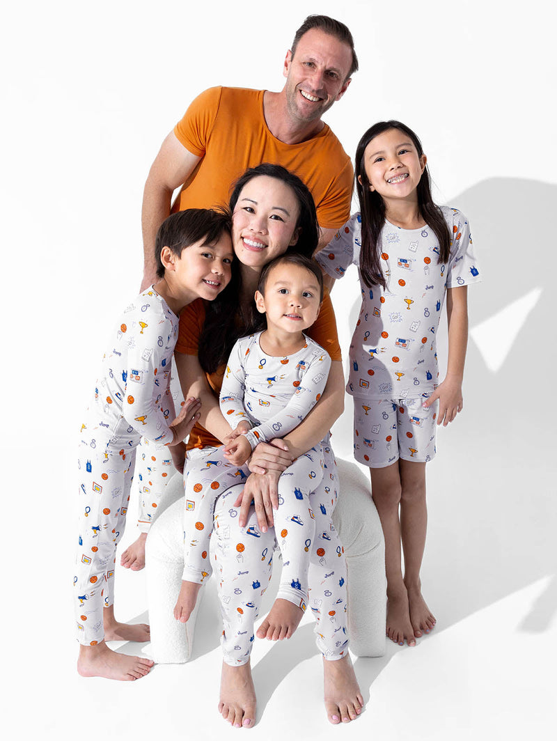 Two adults and three children together in basketball-print pajamas with orange adult tops against a white background.